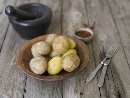 Boiled potatoes in their skins. whole with red pepper, salt and spicy sauce on clay plate, old wooden table, rustic style. Close up, copy space. Top view.の写真素材