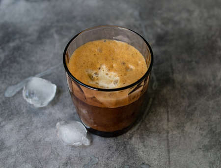 Ice coffee in a tall glass, ice cubes on a gray wooden table. Cold summer drink with tubes on a black background with copy space. Close up.の写真素材