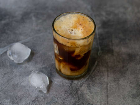Ice coffee in a tall glass, ice cubes on a gray wooden table. Cold summer drink with tubes on a black background with copy space. Close up.の写真素材