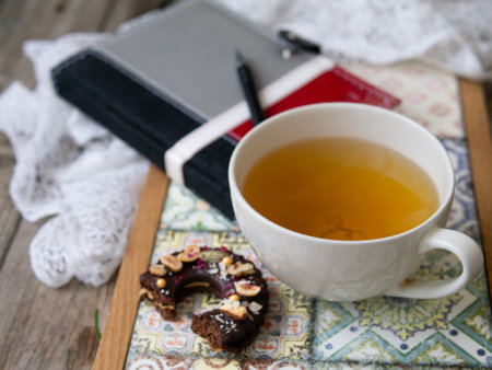 Green tea in big white cup with chocolate cookie on colored tray on a wooden background. Workpiece with notepad and pen. Planning. Breakfast. Close up.の写真素材