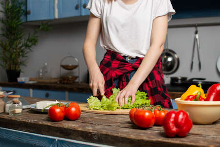 hands of the girl cut lettuce on a wooden table, a woman prepares a veggie salad, healthy food, a knife chops greensの写真素材