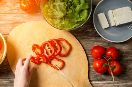 hands of a girl cut bell pepper on a wooden table, the process of making vegetarian salad, close-up cutting of vegetables and greensの写真素材