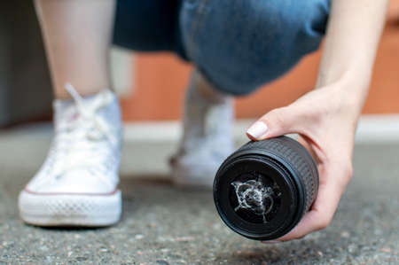 girl photographer dropped a photo lens on the asphalt, glass falls to the ground, close-up of a broken lens on the streetの写真素材