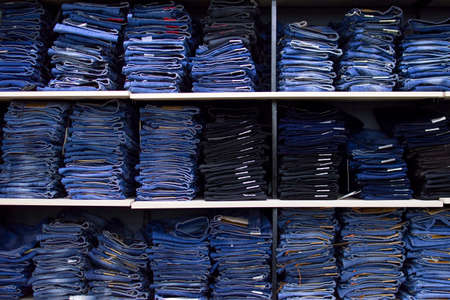 large rack with folded jeans, a lot of jeans, lying on a shelf in the store, textural backgroundの写真素材