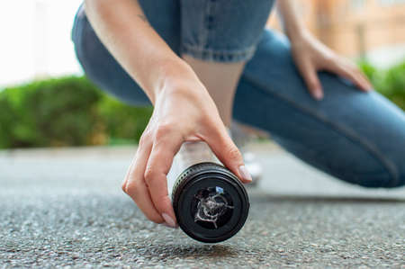 girl photographer dropped a photo lens on the asphalt, glass falls to the ground, close-up of a broken lens on the streetの写真素材