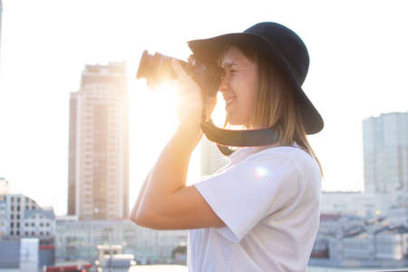 girl photographer with a camera and a tripod against the background of the city, she photographs the sunsetの写真素材