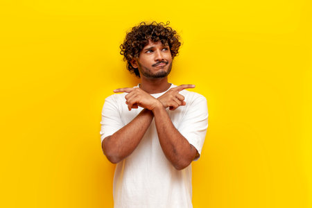 young unsure indian man doubting and pointing with hands at two options on yellow isolated background, puzzled guy thinking and planningの写真素材