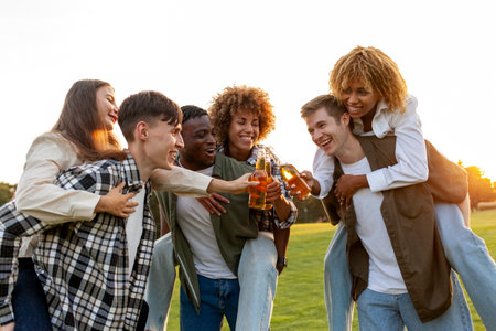 three couples of young multiracial people drinking beer and celebrating toast at party in the park, interracial group of friends drinking alcohol and having fun outdoorsの写真素材