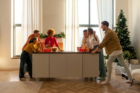 multiracial group of young friends playing beer pong at a New Years party drinking beer and having fun at home, students drinking alcohol and celebrating victory at Christmasの写真素材