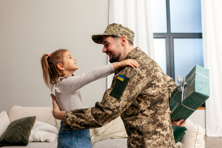 a male Ukrainian military soldier in uniform returned home and hugs his daughter, a patriotic dad gives a gift to the child and celebrates his birthdayの写真素材