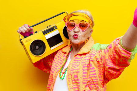 old crazy grandmother in fashionable sportswear listens loudly to music on a tape recorder and takes...