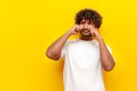 unhappy indian man crying and sad on yellow isolated background, young offended guy in depression and stress upsetの写真素材