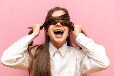 scared little teenage girl with braces closes her eyes and screams on a pink isolated background, child in stress pulls out hair and hidesの写真素材