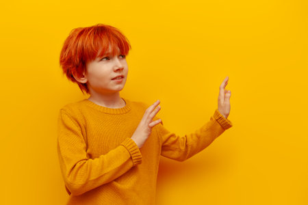 dissatisfied red-haired teenage boy avoids and rejects with his hands on a yellow isolated background, a child with an orange hairstyle shows a gesture of refusal and prohibitionの写真素材