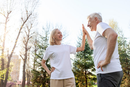 elderly couple of seniors man and woman high-five and rejoice at success in the park outdoors, gray-haired grandparents celebrate victory and play sports in natureの写真素材