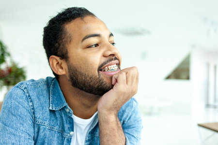 happy african american man with braces smiles and looks away, man in denim shirt takes care of teethの写真素材