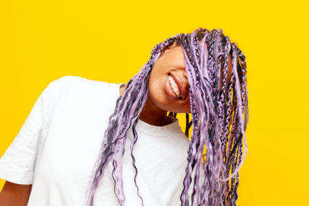 young african american woman with dreadlocks covers her face with her hair and hides on a yellow...