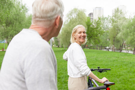 elderly senior couple rides bicycle in the park in the summer and smiles, old gray-haired man and woman are actively resting outdoors, old people practice cycling in forestの写真素材