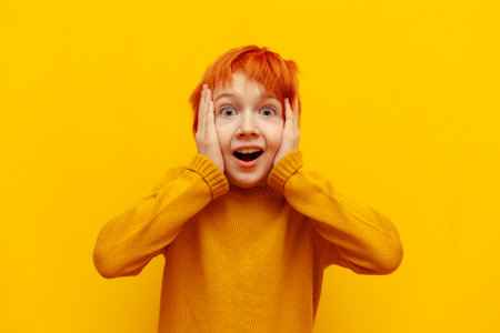 shocked red-haired teenage boy surprised and looking at camera on yellow isolated background,...