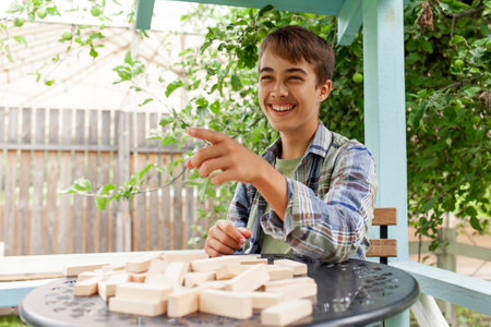 Teenage boy wins board game and makes fun of opponent and points finger, schoolboy competes in Jenga and laughs at loser, kid destroys wooden block towerの写真素材