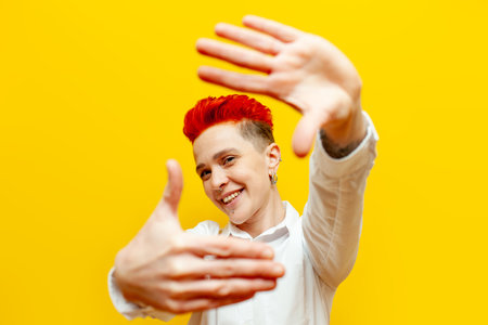young short-haired red-haired girl plans and shows a frame with her hands on a yellow isolated...