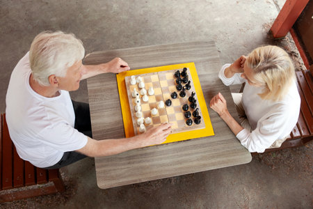 elderly senior couple playing chess outdoors in the park, old man and woman competing in a board game, close-up of hands with pawnsの写真素材
