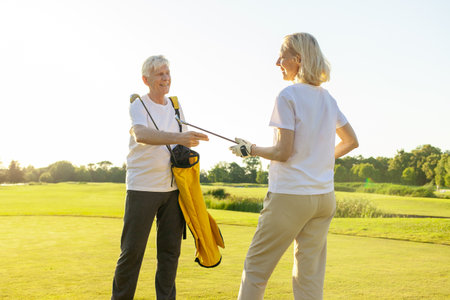 couple of elderly seniors playing golf on the course and smiling, retired grandparents holding golf clubs and putting them in bag, old man and woman doing sports and training outdoorsの写真素材