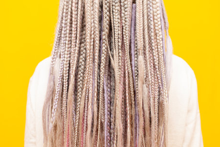 colorful dreadlocks and braids of a girl on a yellow isolated background back view, close-up of a womans unique hairstyleの写真素材