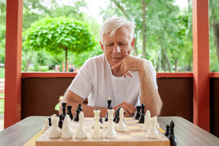 elderly thoughtful senior man playing chess and thinking outdoors in the park, old gray-haired grandfather planning a move in a board gameの写真素材