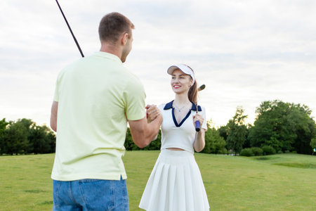 young sporty couple in uniform playing golf on the course and shaking hands, man and woman cheering and competing in golf competition and showing teamwork gestureの写真素材