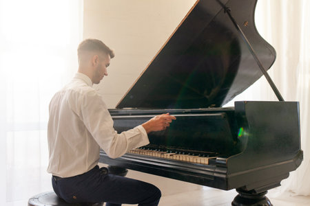 young guy in white shirt plays on old black piano, musician pianist performs melody on acoustic musical instrumentの写真素材