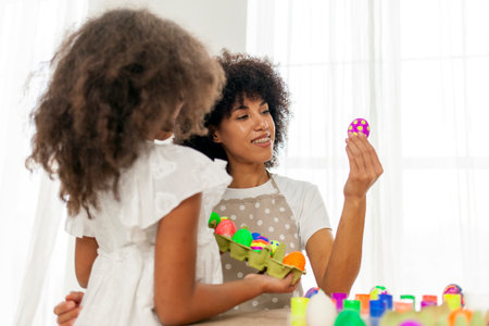 African American mother and daughter celebrate Easter and paint eggs with farbe and brush at home, woman with child decorate Easter eggsの写真素材