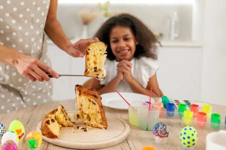 African American mother and daughter celebrate Easter and eat Easter cake at home, woman with child...