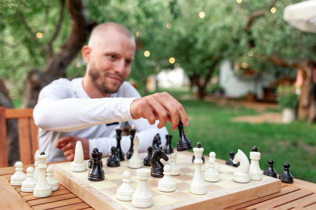 young cheerful guy plays chess outdoors in the park and smiles, the man makes move in the board gameの写真素材