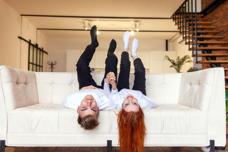young couple in love fooling around at home on the sofa and lying upside down, man and woman having...