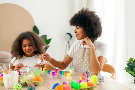African American mother and daughter celebrate Easter and paint eggs with brush at home, woman with child decorate Easter eggsの写真素材