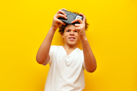 cheerful african american boy in white t-shirt playing video games on smartphone over yellow...
