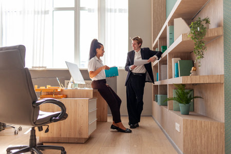 young man in business suit reading report and talking with african american female boss in office,...