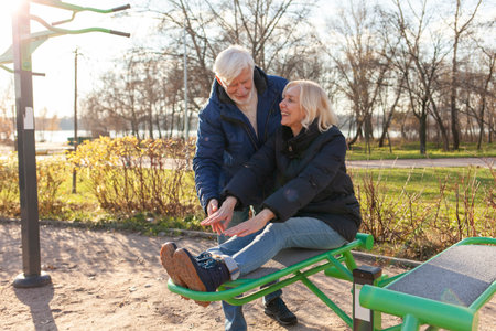 couple of elderly seniors stretch on outdoor exercise equipment, gray-haired husband and wife exercise on playground in parkの写真素材