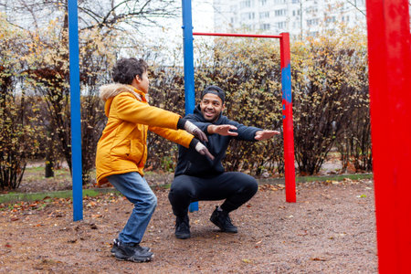 African American man and his son exercise and do exercises outdoors on playground, teenager...
