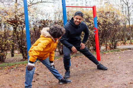 African American man and his son exercise and do exercises outdoors on playground, teenager...
