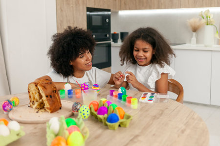 African American mother and daughter celebrate Easter and paint eggs with farbe and brush at home,...