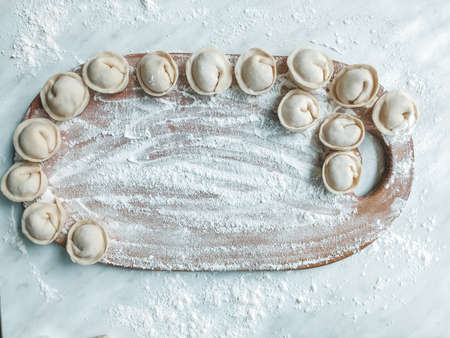 Beautiful dumplings are laid out on the board. In the background is a table covered in flour.