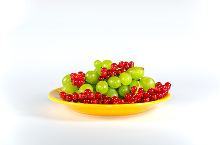 Plate of grapes and red currants on white tableの写真素材