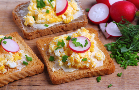 Toasted bread with scrambled eggs with fresh chives and radish for breakfastの写真素材
