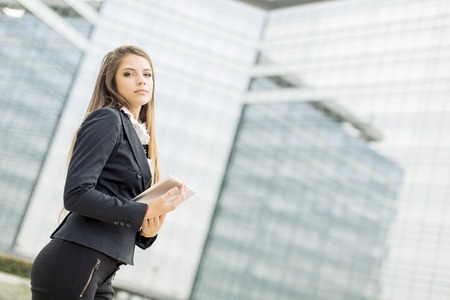 Young businesswoman with tablet in front of office buildingの写真素材