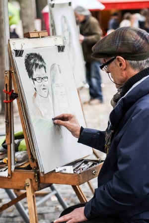 Unidentified man drawing a portrait of the tourist at Place du Tertre at September 16, 2013. Place du Tertre is now an open-air workshop with its 288 official painters.のeditorial素材