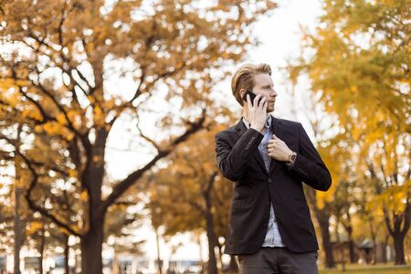 Young man with mobile phone in the autumn parkの写真素材