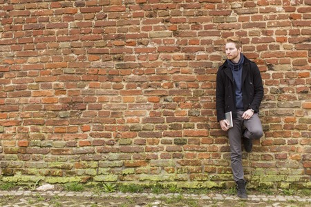 Young man with tablet by the brick wallの写真素材