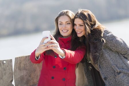 Happy young women taking photo with mobile phoneの写真素材